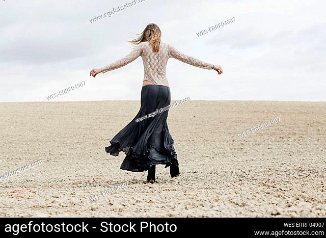 Mid adult woman with arms outstretched walking at beach against sky