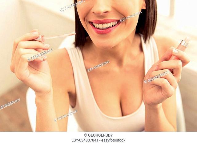 Cropped image of beautiful young woman doing makeup using a lipstick and smiling