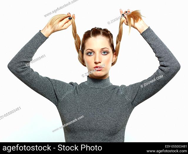 Portrait of beautiful young dark blonde woman. Female with creative braid hairdo on gray background. Girl holds braids in hands
