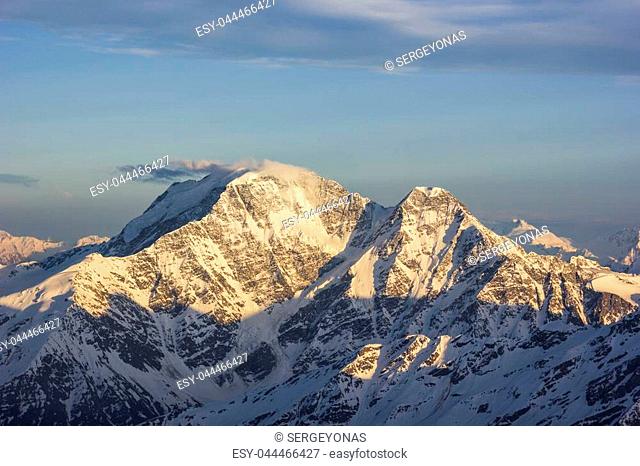 snowy Caucasus mountains with glaciers at sunset from elbrus slopes with stones and clouds on blue sky