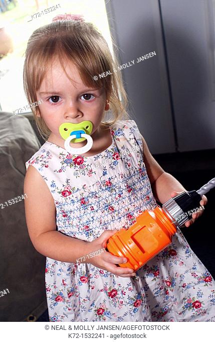 Little girl with pacifier holds a toy drill