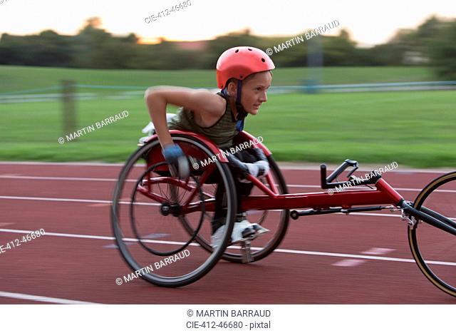 Determined teenage girl paraplegic athlete speeding along sports track in wheelchair race