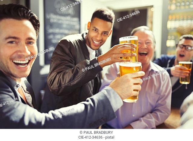 Enthusiastic men friends toasting beer glasses at bar