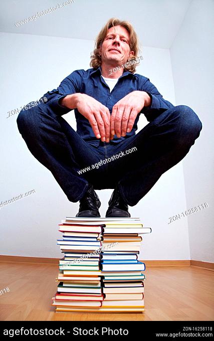 Mann hockt auf einem Stapel Bücher