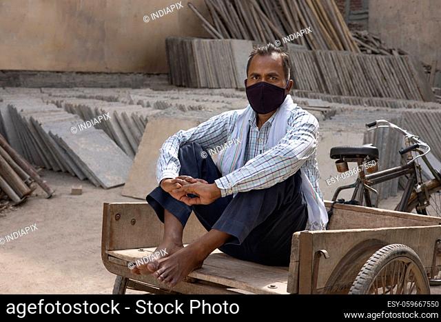 A DAILY WAGE LABOURER LOOKING AT CAMERA WHILE SITTING ON CART