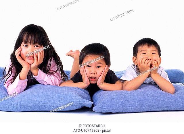 Three children lying on Blue Pillows, putting elbows on pillows, Resting their Faces on their Hands, Looking at Camera, Front View