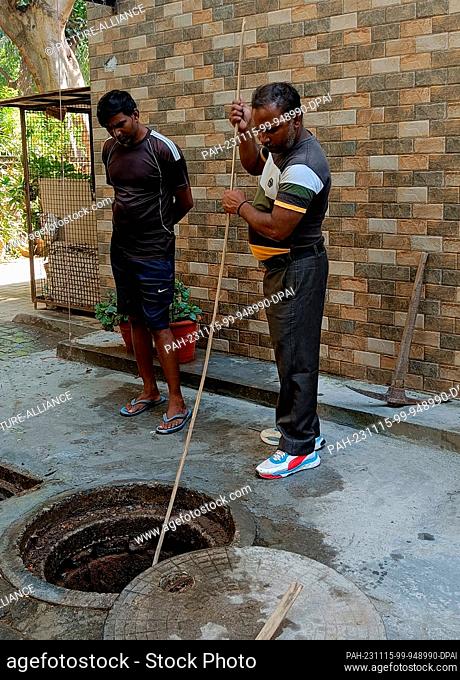 PRODUCTION - 03 October 2023, India, Neu-Delhi: Vinod and Kuldeep open a manhole and remove sludge from a sewer in a residential area in South Delhi