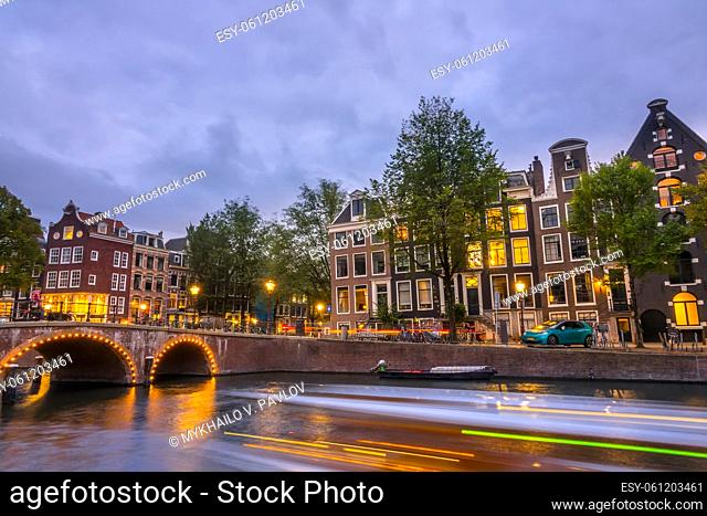 Netherlands. Evening on the Amsterdam canal. Old stone bridge and typical houses on the embankment. Traffic on the water and streets