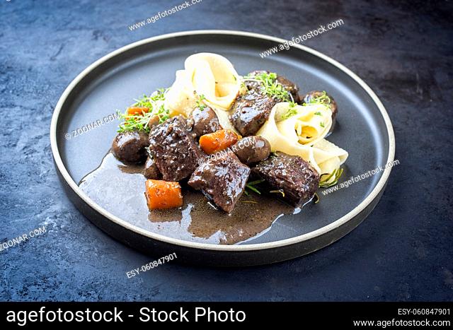 Modern style traditional French boeuf bourguignon with tagliatelle noodles in red wine sauce served as close-up in a Nordic design plate