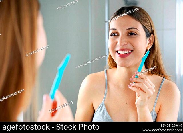 Close up of beautiful woman holding razor for facial hair removal in bathroom at home