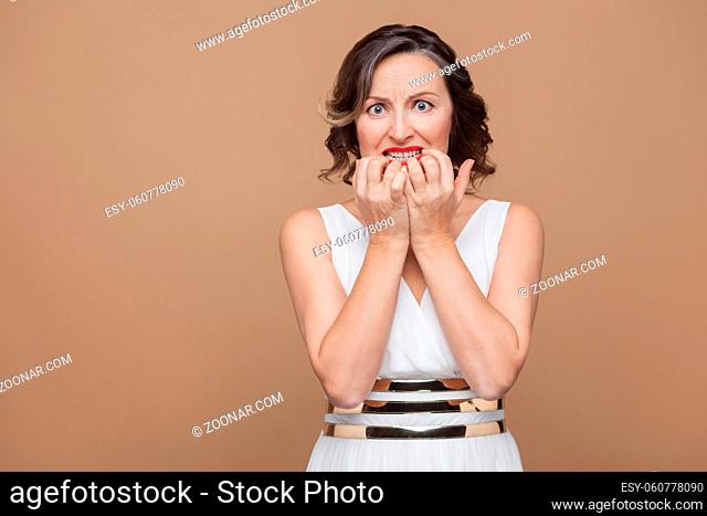Nervous, sad or shocked and worried middle aged woman. Emotional expressing woman in white dress, red lips and dark curly hairstyle