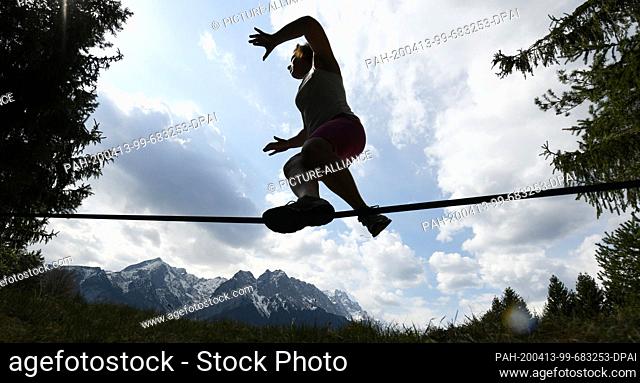 13 April 2020, Bavaria, Garmisch-Partenkirchen: A young woman is balancing on a slackline, the Wettersteingebirge can be seen in the background
