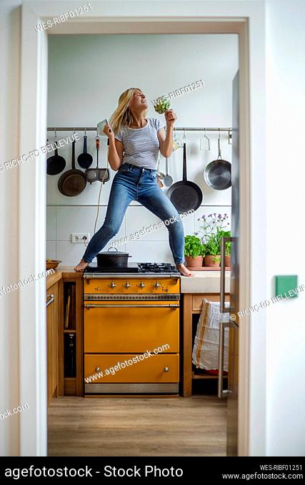 Carefree woman standing on stove enjoying dancing in kitchen