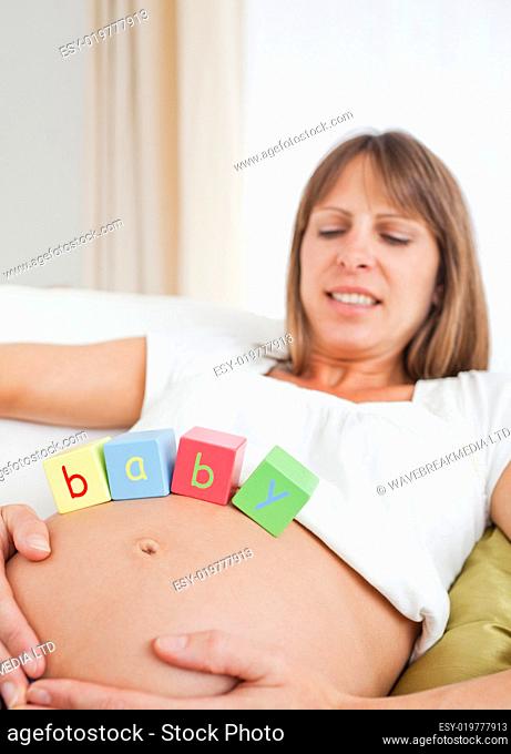 Beautiful pregnant female playing with wooden blocks while lying
