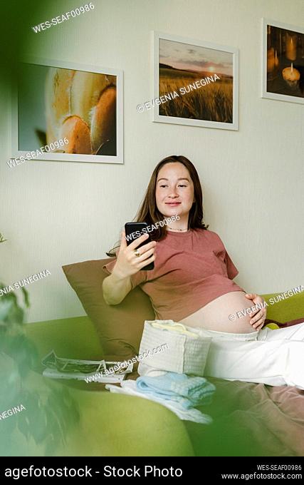 Smiling pregnant woman using mobile phone at home
