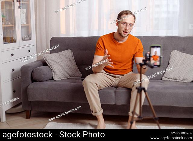 Cheerful middle-aged bearded man blogger broadcasting from home, using smartphone and tripod