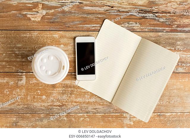 business, education, objects and technology concept - close up of notebook, coffee paper cup and smartphone on table