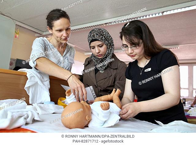 Vocational school teacher Ivonne Schroeter (l-r) explains how to change diapers to students Rasha and Hadia from Syria in the course 'Personal hygiene and...