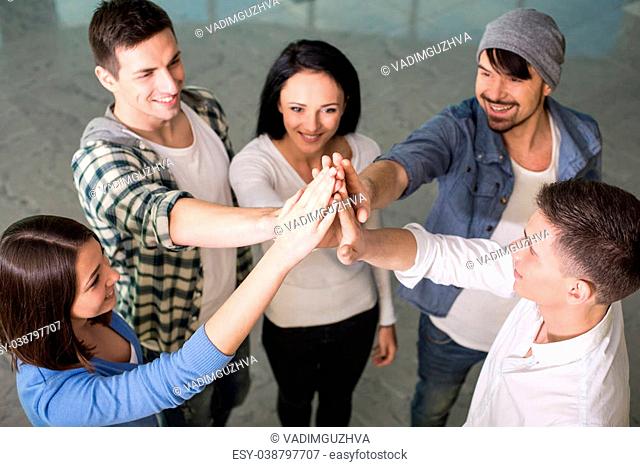 Group of cheerful young people are standing close to each other and holding hands up