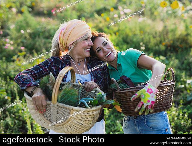 Happy gardener leaning on colleague standing with vegetable basket at field