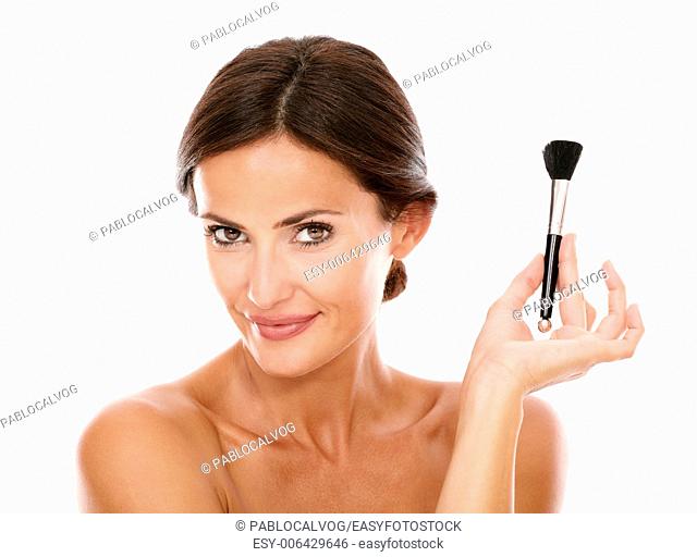 Smiling hispanic woman with make up brush for smooth her face and nude shoulders while looking at camera on isolated studio