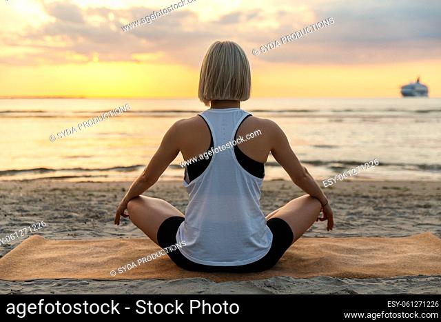 woman meditating in lotus pose on beach