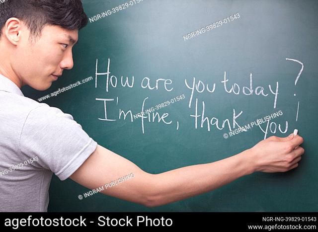 Young man writing English sentences on the blackboard