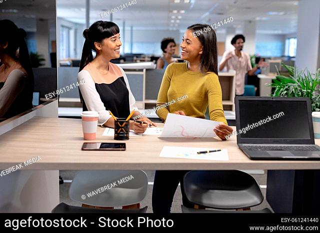 Happy multiracial businesswomen discussing over document while working together at modern workplace