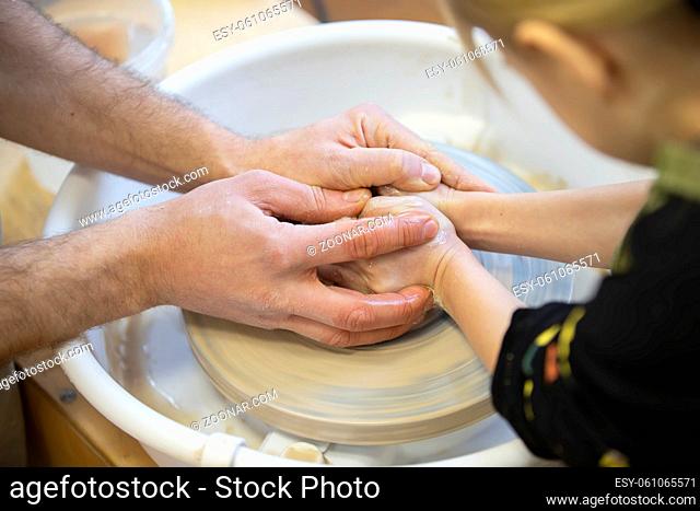 The potter teaches the craft to the child. Close-up of a potter's hands and a child's hand with a product on a potter's wheel. Working with clay