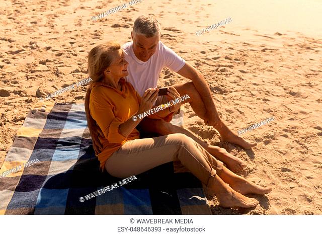 Senior couple reviewing through photos on mobile phone at beach