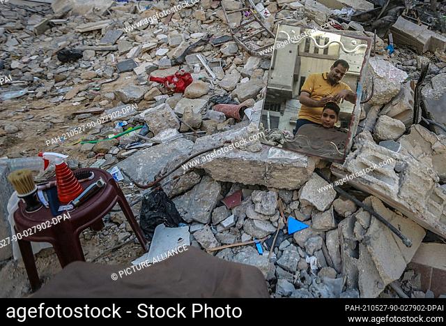 27 May 2021, Palestinian Territories, Gaza City: Palestinian barber Muhammad al-Sayed is seen reflected while working on the rubble of his barber shop in Beach...