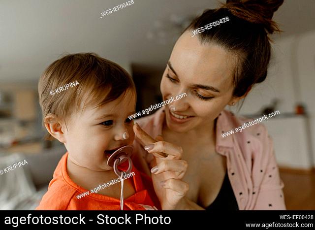 Smiling mother applying cream on nose of daughter at home