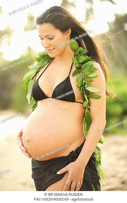 Pregnant girl wearing black bikini and green leaf lei, holding tummy