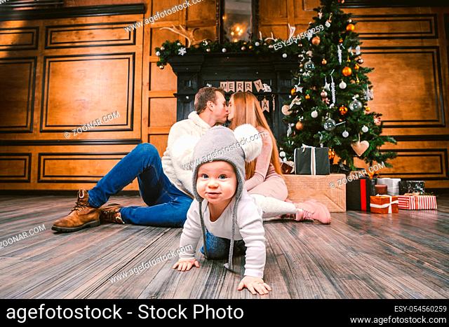 theme family holiday New Year and Christmas. Young caucasian family mom dad son 1 year sit wooden floor near fireplace christmas tree on Christmas evening