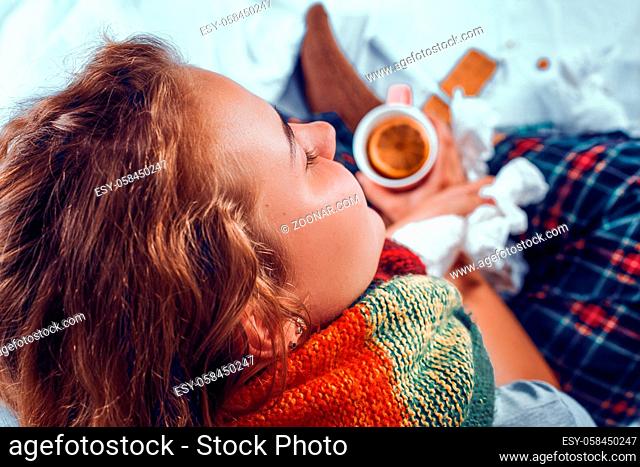 Portrait of right part of woman's face with a coloured woolen scarf holding a cup of hot black tea and sitting in bed while being sick