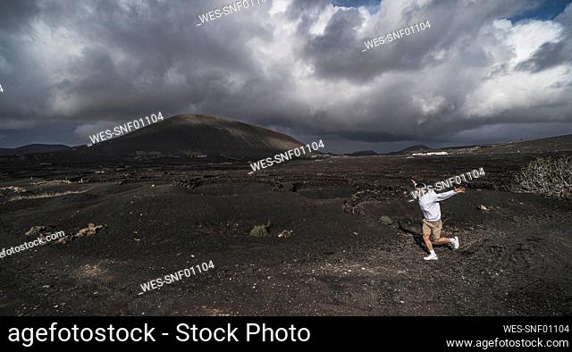 Cheerful male tourist running on black soil at El Cuervo Volcano, Lanzarote, Spain