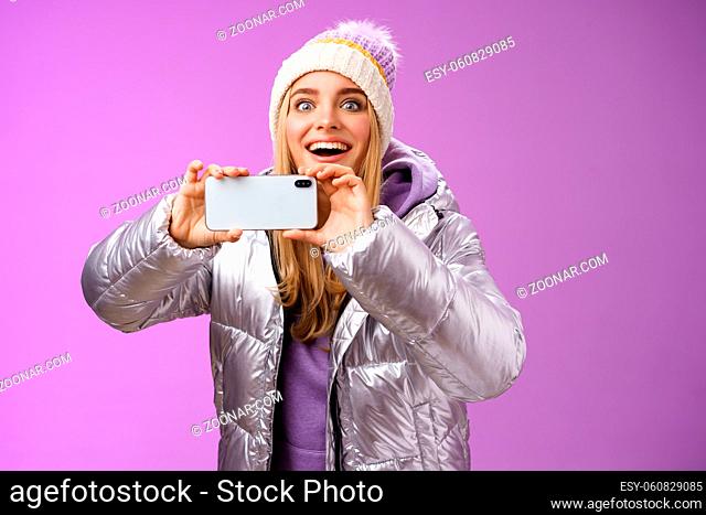 Amused fascinated female in silver jacket head smiling astonished excited look forward holding smartphone recording video taking shots famous person mobile...