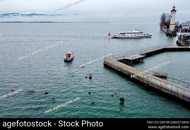 09 December 2023, Bavaria, Lindau (Bodensee): Swimmers swim along the quay wall. On the Saturday after St. Nicholas Day, the now traditional St