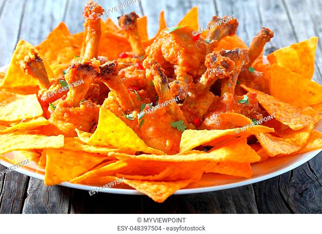deep fried battered crispy chicken wing lollipops sprinkled with parsley and finely chopped chilli with tortilla chips on a white plate on dark wooden table
