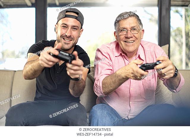 Happy grandfather and grandson playing video game on couch at home