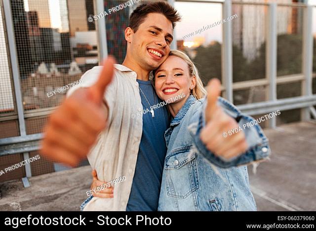happy young couple showing thumbs up on roof top