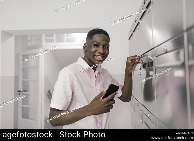 Smiling man with smart phone by mailbox