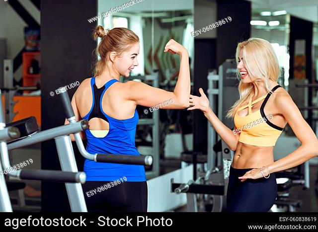 Two athletic blond women talking in the gym. Girl communicates with the trainer
