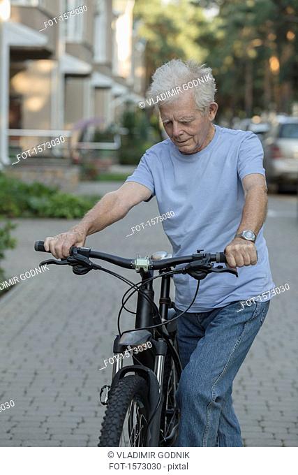 Senior man cycling on cobbled street in city