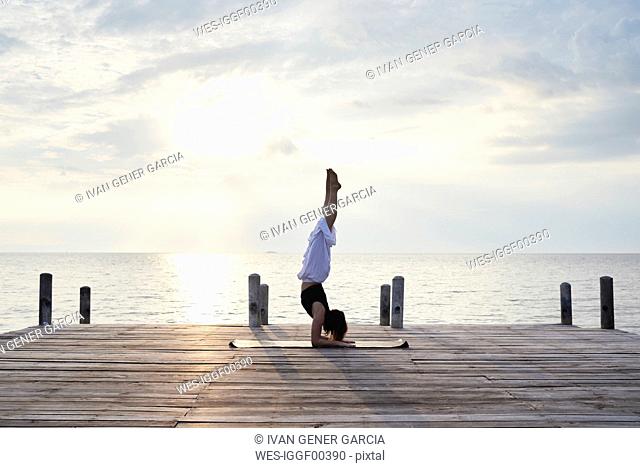 Young woman practicing yoga on a jetty by the sea at sunset