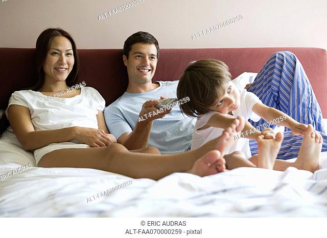 Family watching TV together in bed