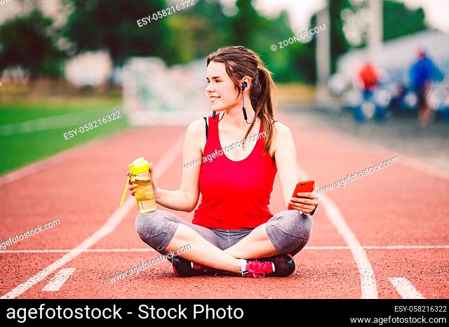 beautiful fitness girl uses smartphone at stadium after workout. Sports and healthy. Sport woman use of cellphone inside sport complex