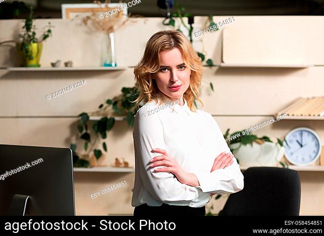 Beautiful businesslady posing on camera in modern office. Crossing hands