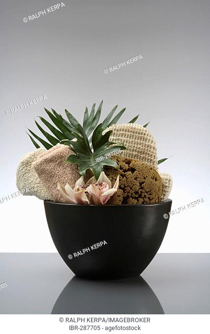 Orchid and palm leaf with towel, sponge and massage glove in a stone bowle
