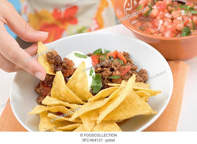Hand dipping tortilla chip in mince sauce, salsa at side